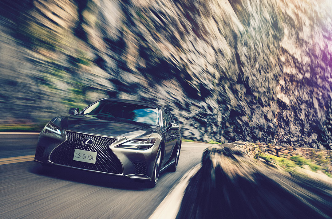 A front-on view of the Lexus LS as it is driven across a road with a rocky background.
