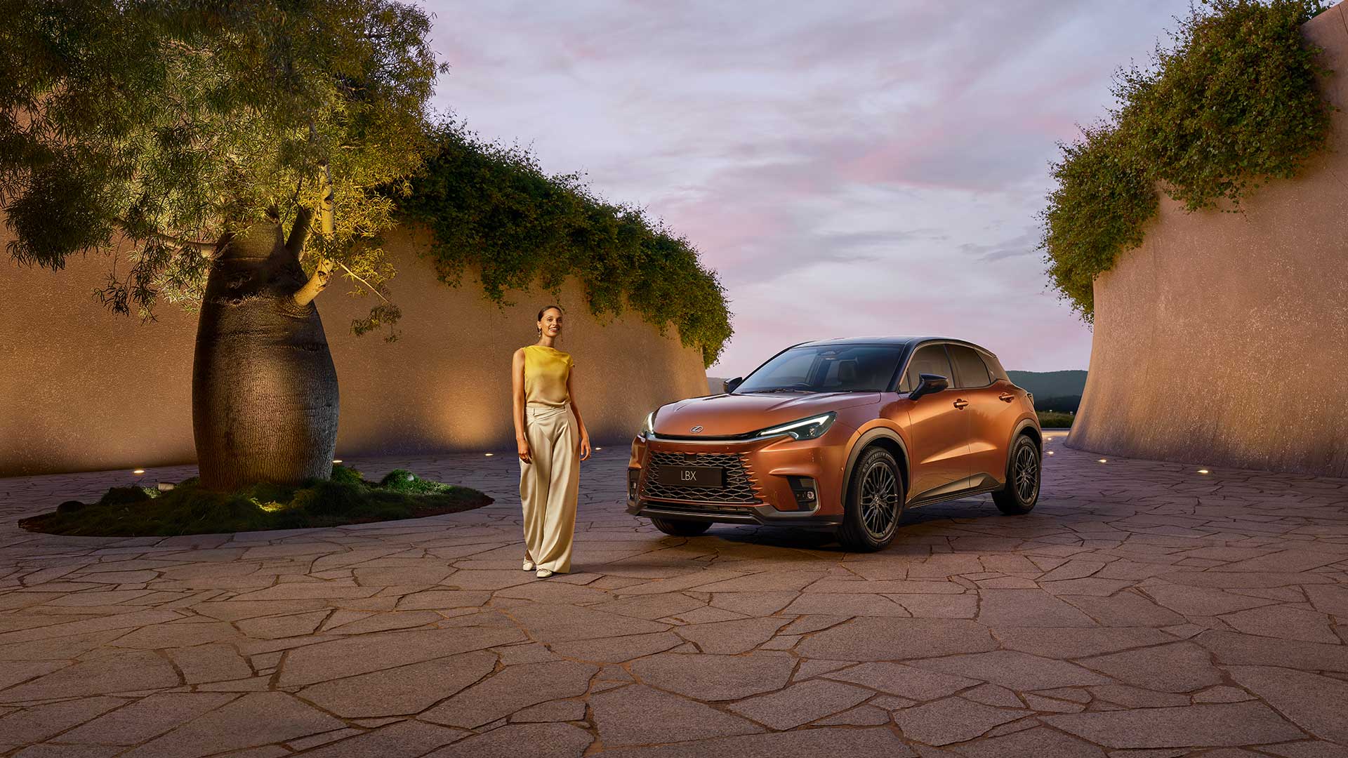A woman is standing between a car and a tree outside.