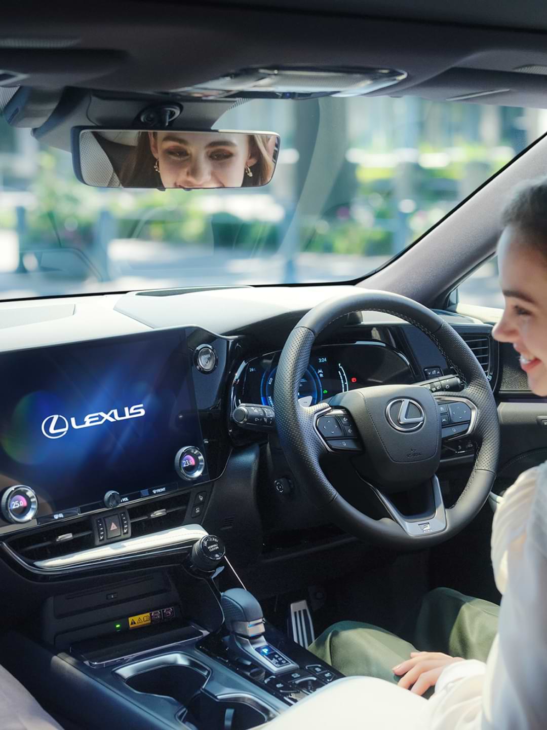 Woman sits behind the wheel of a Lexus NX, the multimedia screen is lit up with "Lexus" written across it.