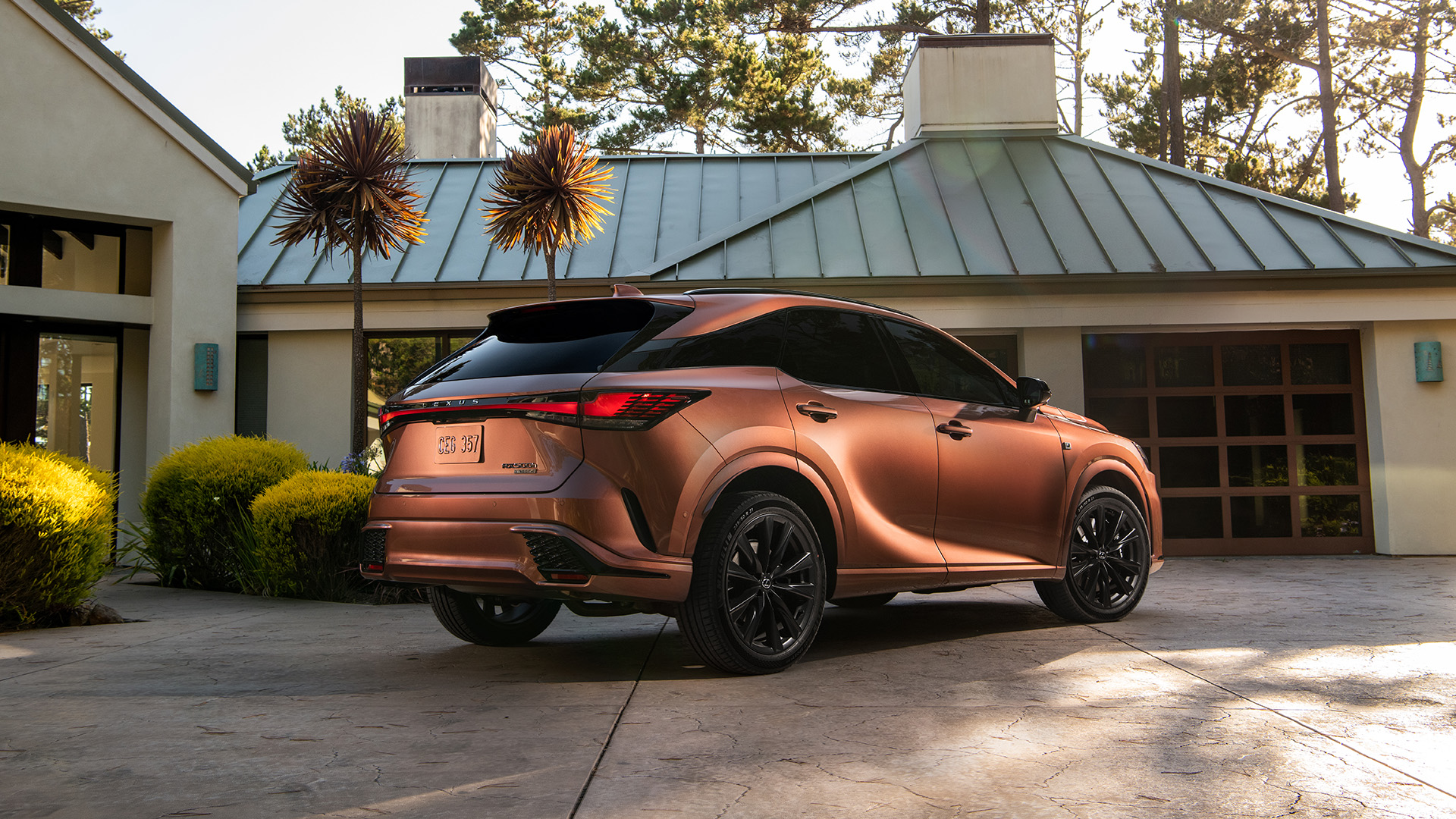 A copper coloured RX is parked in front of a luxury home. 