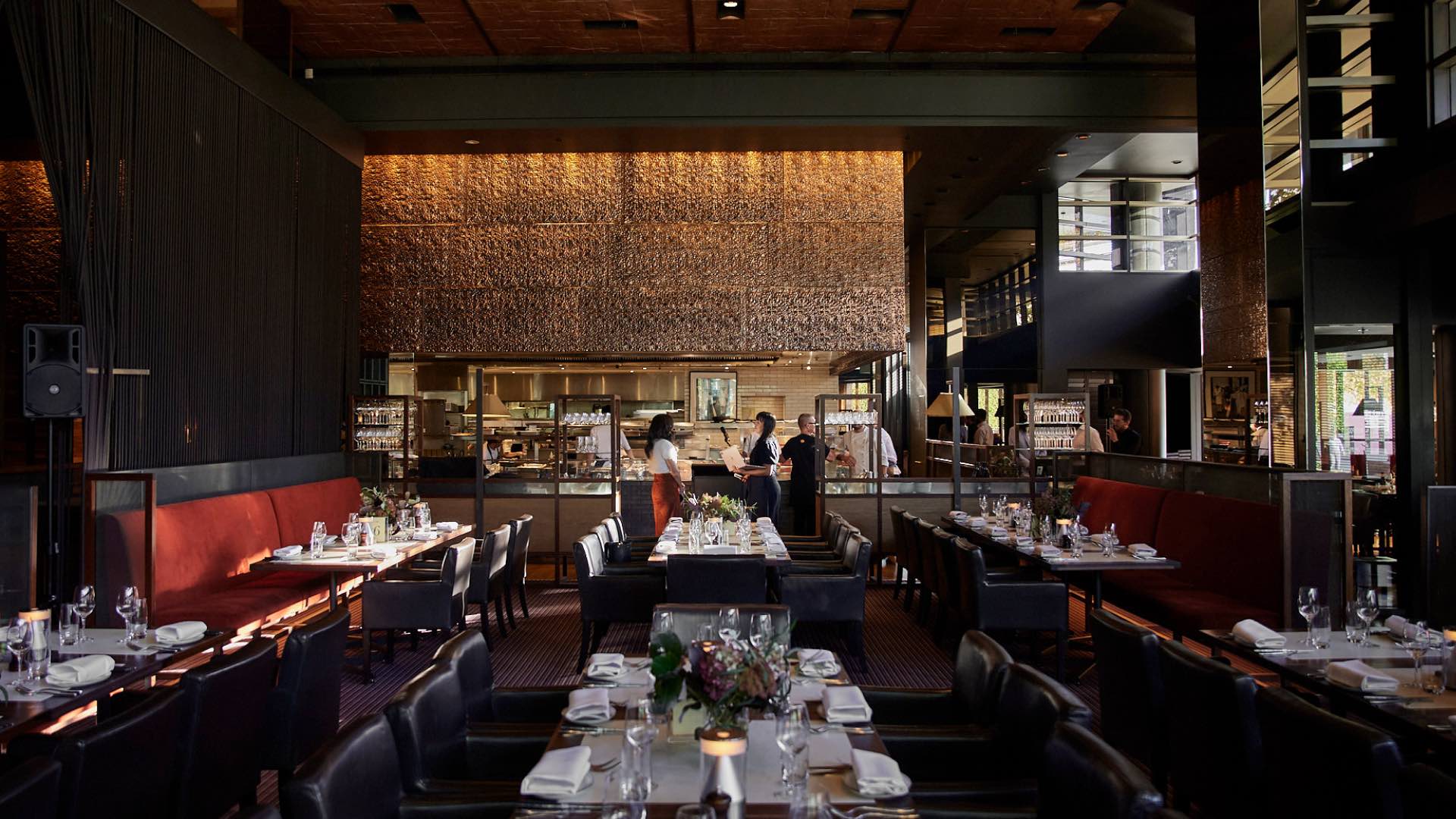 The inside of Rockpool Bar & Grill, lights adorn the back wall. Tables are all set with plates, cutlery and glasses, with lights and flowers.