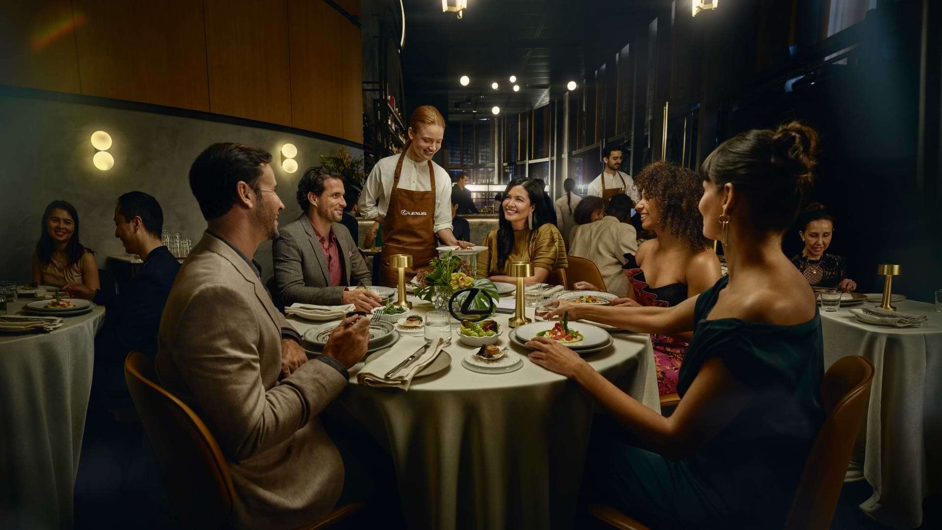 A group of friends are seated at a restaurant table and are smiling at the waiter filling their wine glasses