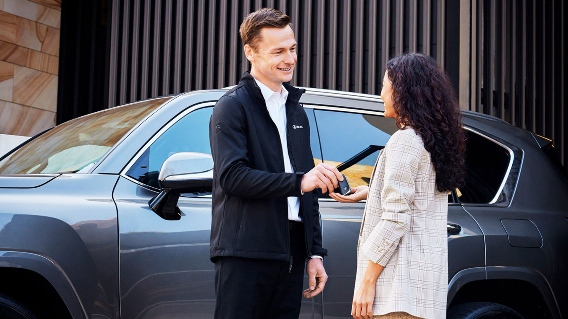 A man gives a woman a pair of keys in front of a Lexus SUV