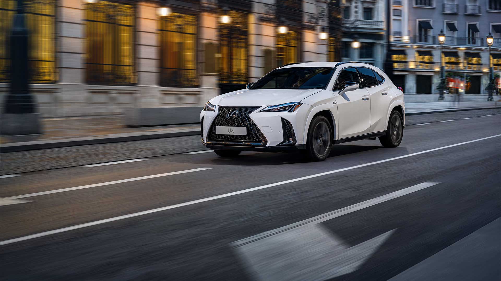 A white 2022 Lexus UX drives down a city street lined with heritage buildings