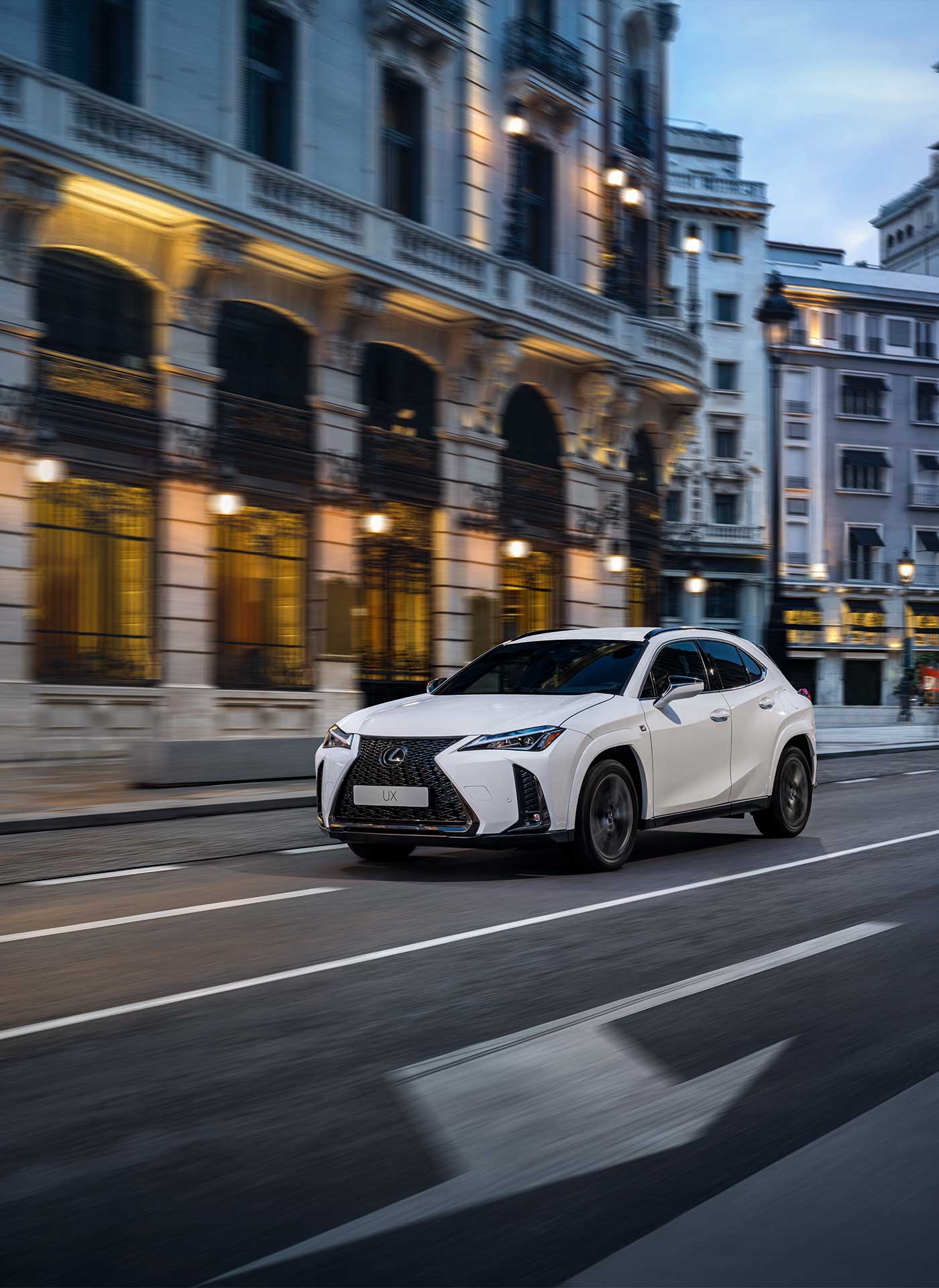 A white 2022 Lexus UX drives down a city street lined with heritage buildings