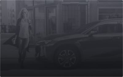 A woman stands next to a Lexus car on an urban street.