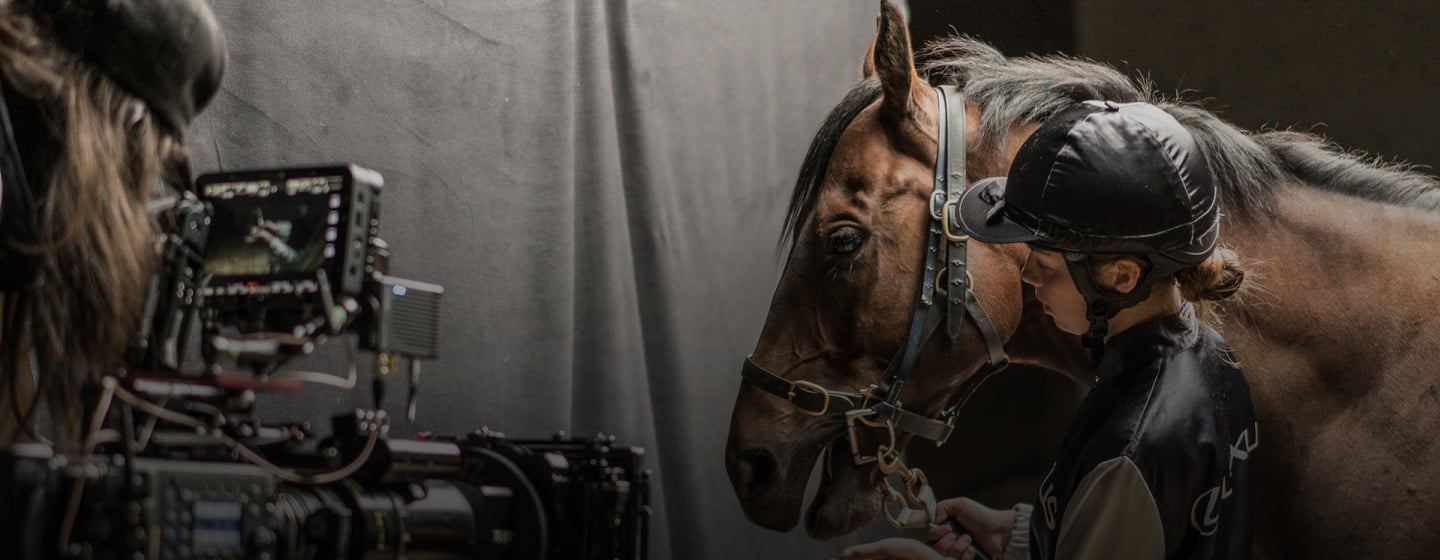 A handler stands beside a bridled horse during a behind-the-scenes film shoot.